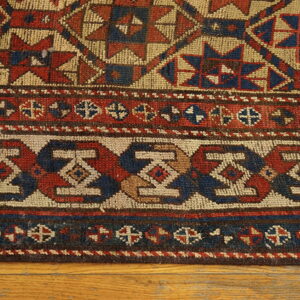 Geometric rug featuring red, blue, and tan tribal patterns and complex border designs on wood floors.
