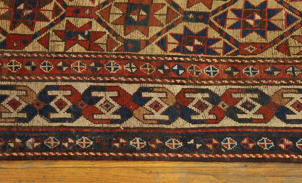 Geometric rug featuring red, blue, and tan tribal patterns and complex border designs on wood floors.