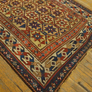 Red, blue, and tan geometric rug with star motifs lies diagonally across worn wood flooring.