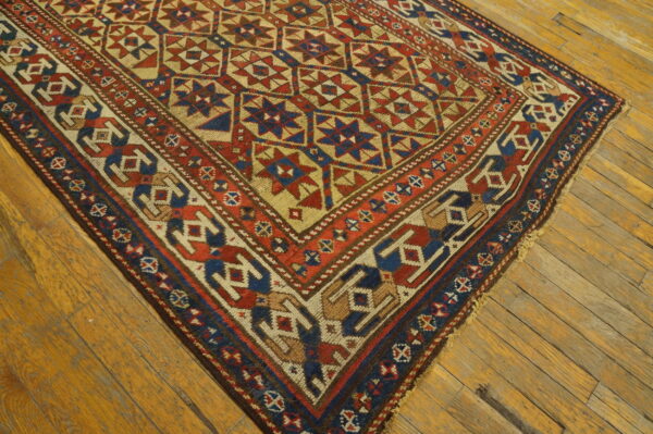Red, blue, and tan geometric rug with star motifs lies diagonally across worn wood flooring.