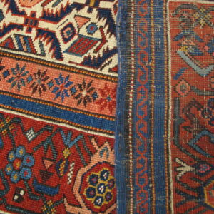 Complex red, navy, and cream tribal patterns meet a flat woven blue and rust stripe border.