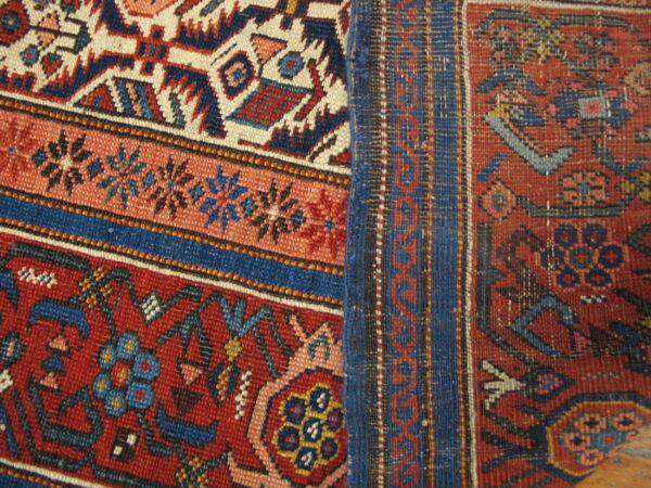 Complex red, navy, and cream tribal patterns meet a flat woven blue and rust stripe border.