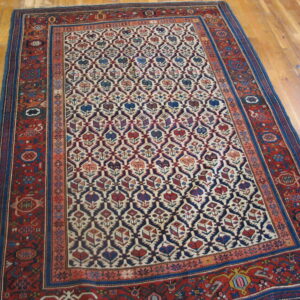 Red, navy, and cream low-pile rug with repeating stylized floral motifs on wood planks.