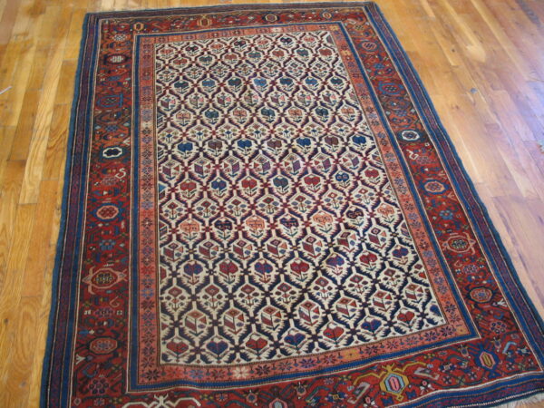 Red, navy, and cream low-pile rug with repeating stylized floral motifs on wood planks.