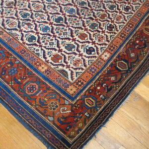 Close-up of a red, blue, and cream geometric rug with layered borders on a light wood floor.