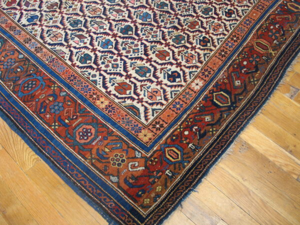 Close-up of a red, blue, and cream geometric rug with layered borders on a light wood floor.