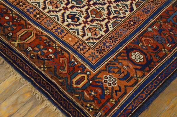 Detailed corner of a traditional rug featuring rust, navy, and cream geometric motifs on a wood floor.