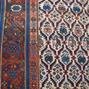 Low-pile rug close-up showing complex blue, rust, and cream geometric motifs on wood floor.