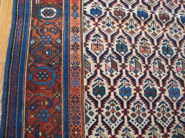 Low-pile rug close-up showing complex blue, rust, and cream geometric motifs on wood floor.