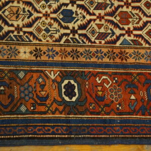 A detailed view of a rug featuring blue, rust, and beige geometric patterns and dense borders.