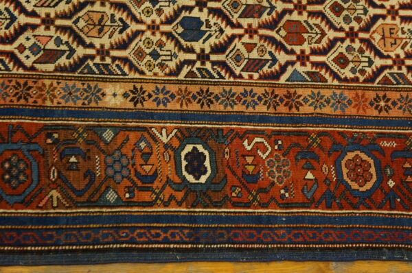 A detailed view of a rug featuring blue, rust, and beige geometric patterns and dense borders.