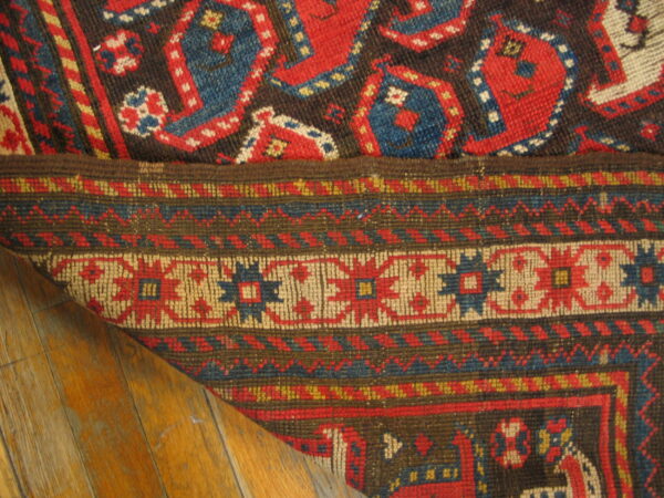 Close-up of a red, blue, and brown geometric rug folded on distressed wooden flooring.