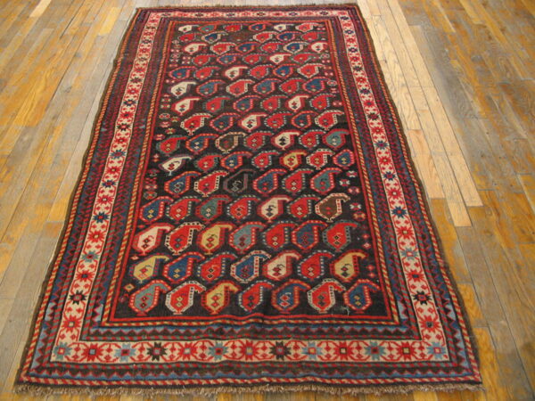 Dark rug with red, blue, and cream boteh patterns and geometric borders on light wood floorboards.