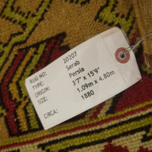 Gold, red, and olive geometric patterned rug with a white product tag tied to the surface.