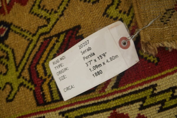 Gold, red, and olive geometric patterned rug with a white product tag tied to the surface.