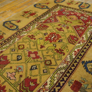 Gold area rug with red, green, and navy traditional geometric patterns rests on highly distressed wood planks.