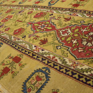 Golden yellow low-pile rug with intricate red, green, and blue geometric patterns on light wood flooring.