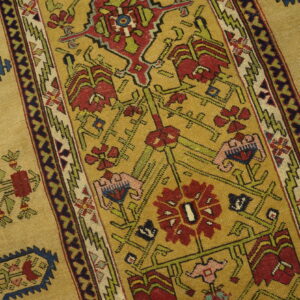 A golden patterned rug features red, green, and blue geometric motifs next to light wooden flooring.