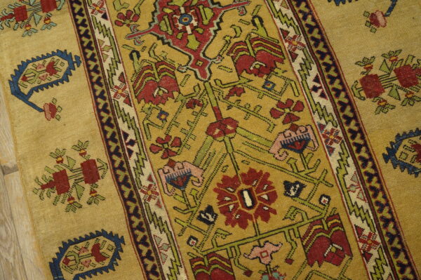 A golden patterned rug features red, green, and blue geometric motifs next to light wooden flooring.