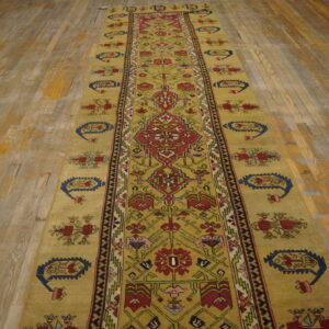 A long mustard runner rug with geometric red and blue patterns covers a distressed wood floor.