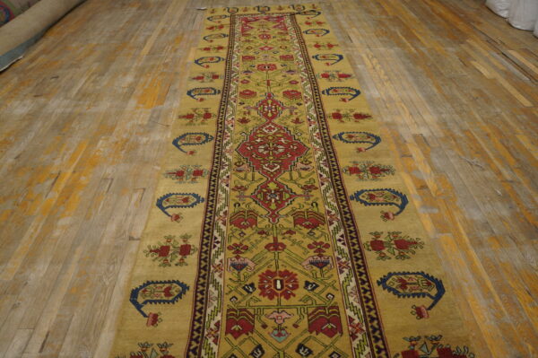 A long mustard runner rug with geometric red and blue patterns covers a distressed wood floor.