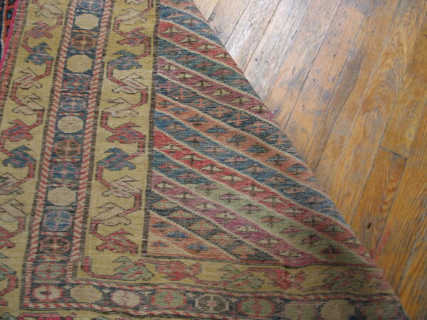 A yellow, red, and blue flat-woven rug featuring vertical borders and diagonal stripes covers wood flooring.