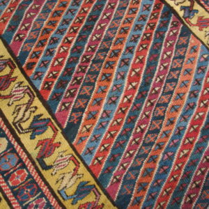 Close-up of a brightly colored rug with diagonal striped patterns and a yellow border displaying stylized geometric figures.