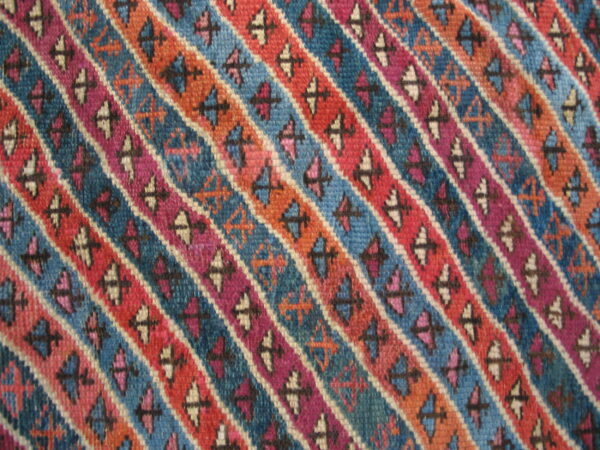 Rug detail with repeating diagonal stripes in vibrant blue, red, purple, and orange geometric designs.