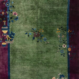 Lush green pile rug with magenta and plum borders decorated with colorful floral and vessel designs.