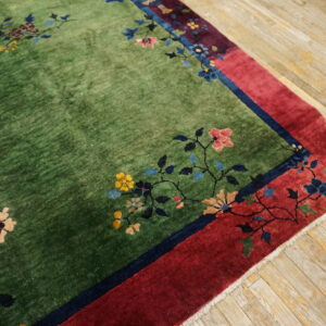 Green pile rug with multicolored floral designs and a wide red border on distressed wooden flooring.