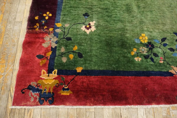 Plush green rug with a red border and floral patterns on worn wood flooring, viewed closely.