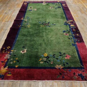 Green floral rug with maroon and red borders displayed on distressed wooden plank flooring.
