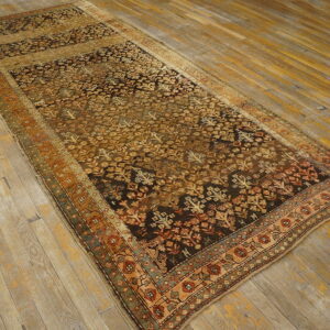 A distressed runner rug with a dense gold and dark brown floral pattern on aged wooden floors.