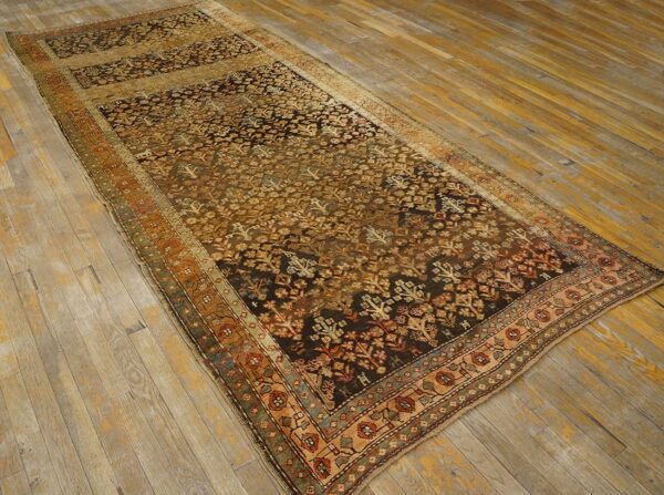 A distressed runner rug with a dense gold and dark brown floral pattern on aged wooden floors.