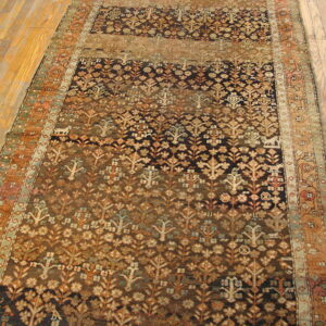 Rust and brown runner rug with dense floral and tree patterns lying on light wood planks.