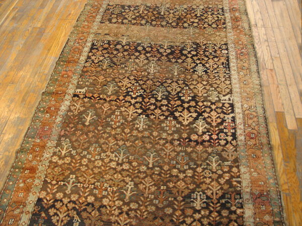 Rust and brown runner rug with dense floral and tree patterns lying on light wood planks.