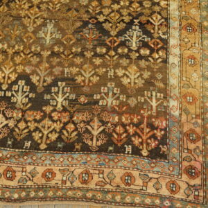 Dark brown patterned rug with tan and rust floral motifs and a complex border rests on yellow plank flooring.