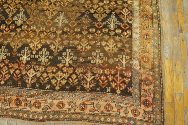 Dark brown patterned rug with tan and rust floral motifs and a complex border rests on yellow plank flooring.