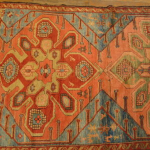 Geometric central medallion rug featuring orange, teal, and beige patterns on wood planks.