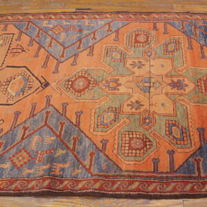 Low-pile geometric rug in rust, dusty blue, and green on light brown hardwood flooring.