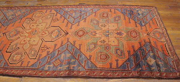 Low-pile geometric rug in rust, dusty blue, and green on light brown hardwood flooring.