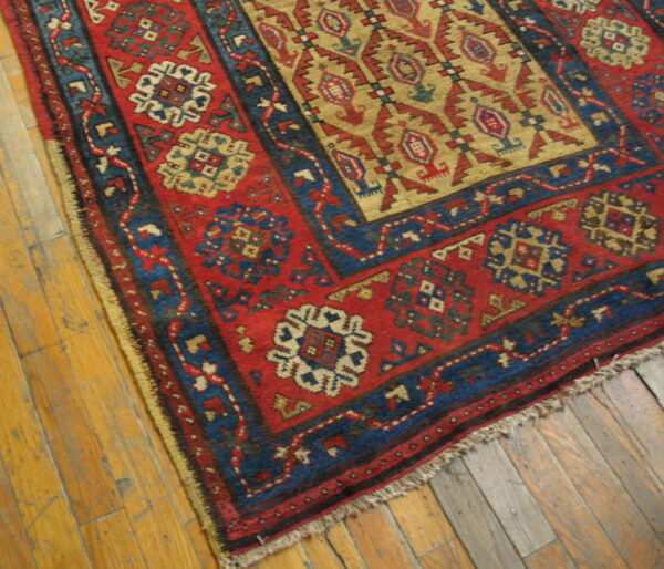 Red, blue, and tan tribal rug corner with geometric patterns resting on worn wood flooring.