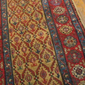 Close-up of a high-pile red, gold, and blue geometric runner rug on light brown hardwood flooring.