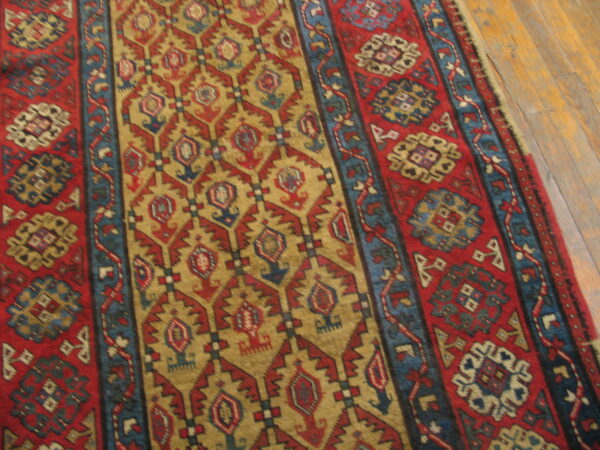 Close-up of a high-pile red, gold, and blue geometric runner rug on light brown hardwood flooring.