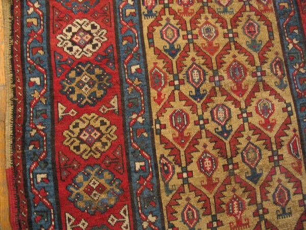 Close-up of a geometric rug featuring red floral panels and tan fields with blue and red motifs.