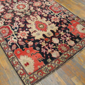 Low-pile rug with intricate red, cream, and dark blue traditional patterns rests on distressed hardwood flooring.