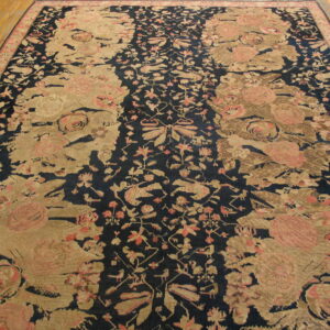 Low-pile rug with large tan and pink floral patterns on a dark navy field over hardwood flooring.