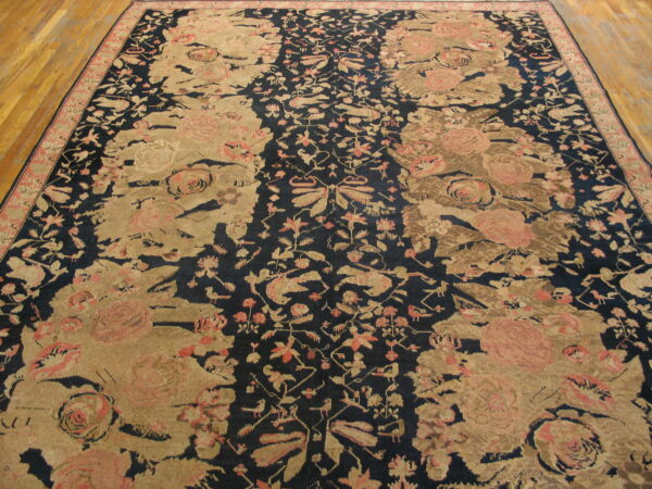 Low-pile rug with large tan and pink floral patterns on a dark navy field over hardwood flooring.