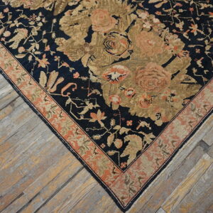 Dark blue rug corner with gold and pink botanical patterns rests on distressed gray-washed wooden planks.