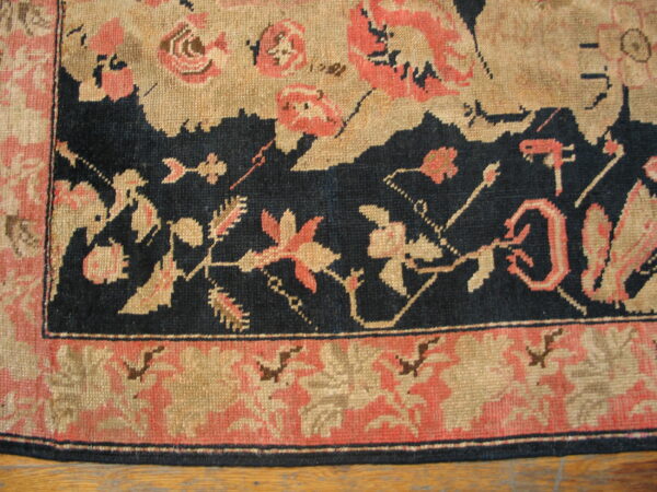 Detail of a low-pile rug showing a navy, tan, and coral floral border on wood flooring.
